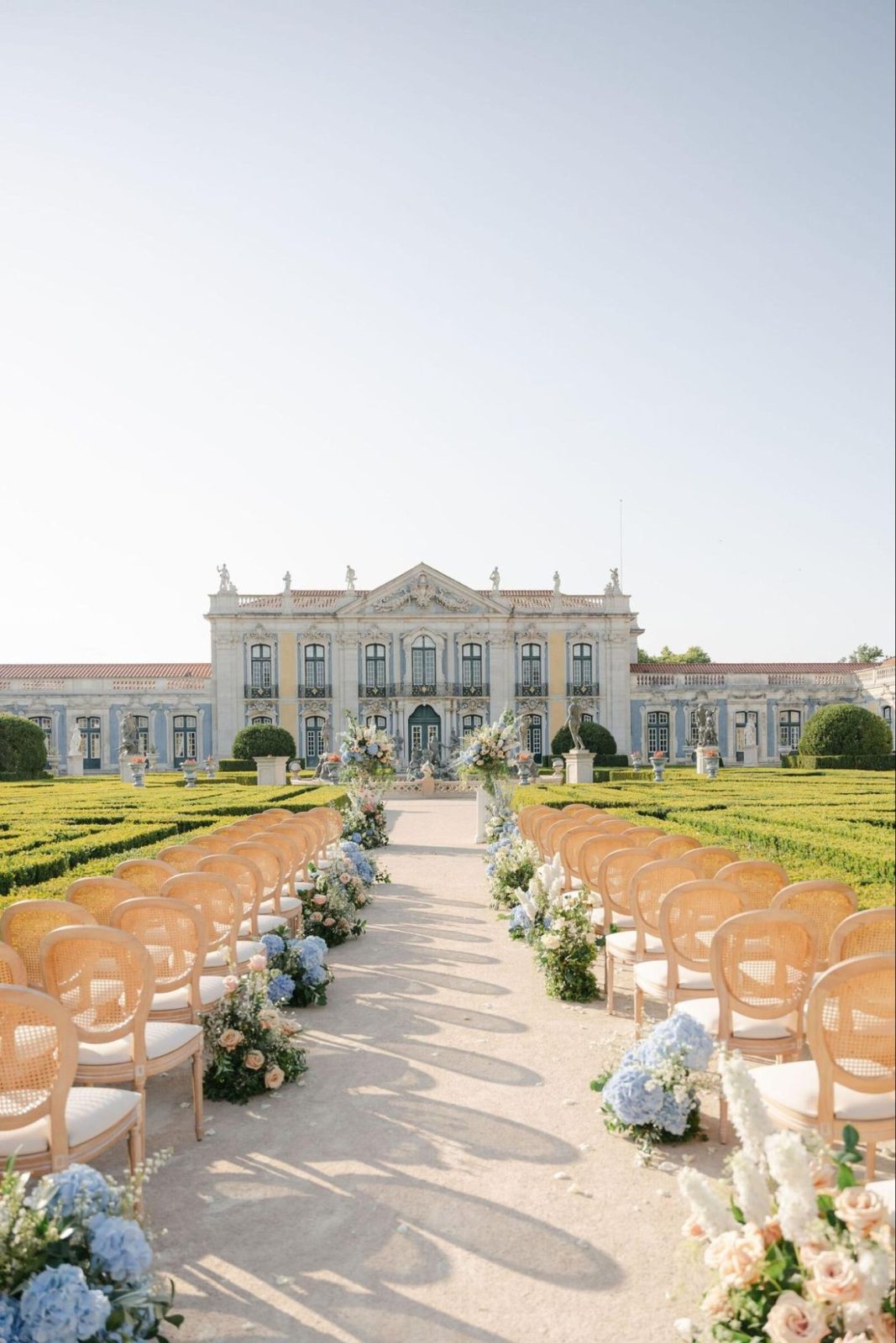 Ceremony chairs lining a gravel aisle through formal gardens towards a blue and white palace in Portugal