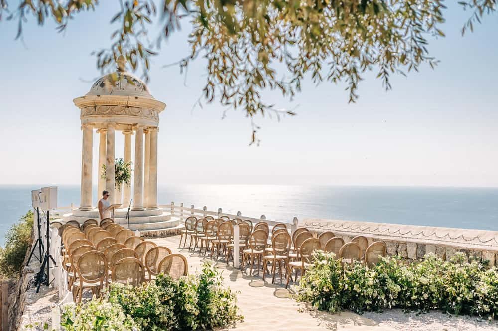 Rattan chairs set up beside a stone temple on a cliff above the sea in Mallorca